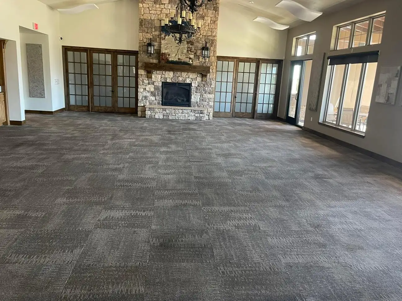 Large commercial room with cleaned gray carpet, stone fireplace, multiple glass doors and windows for office cleaning