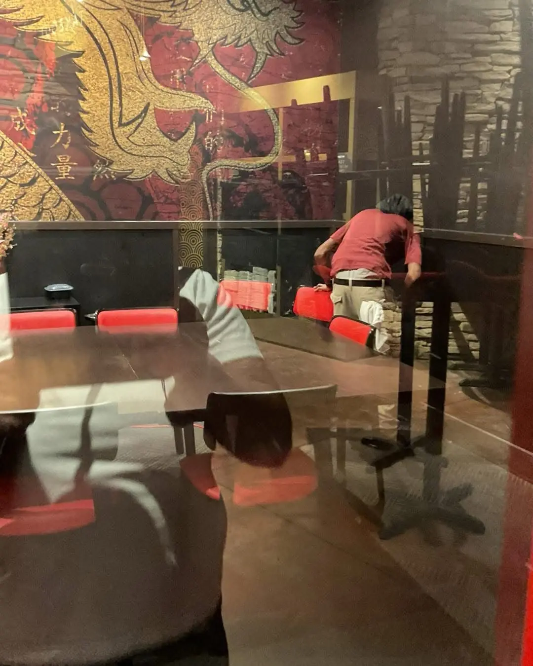 A cleaner performs commercial dining room deep cleaning in a restaurant booth area with dragon mural and red chairs