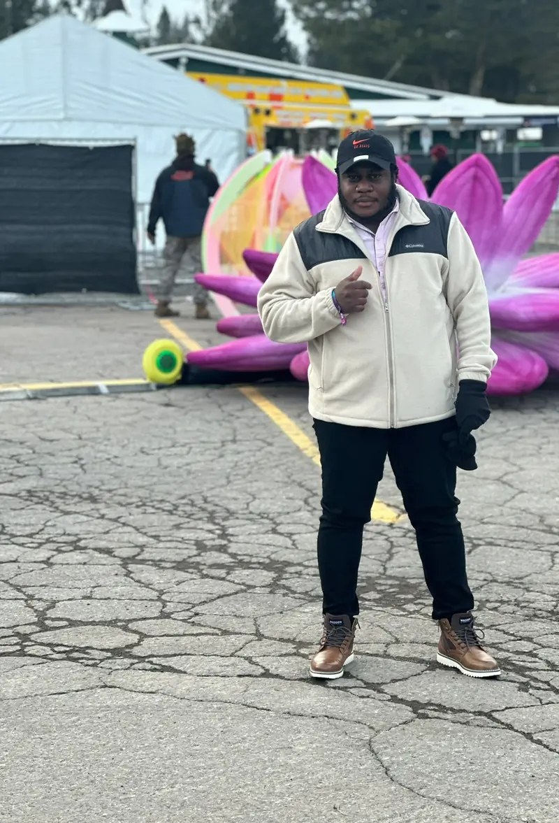 Yardie Cleaning founder standing outdoors at an event giving a thumbs up in front of colorful inflatable decor