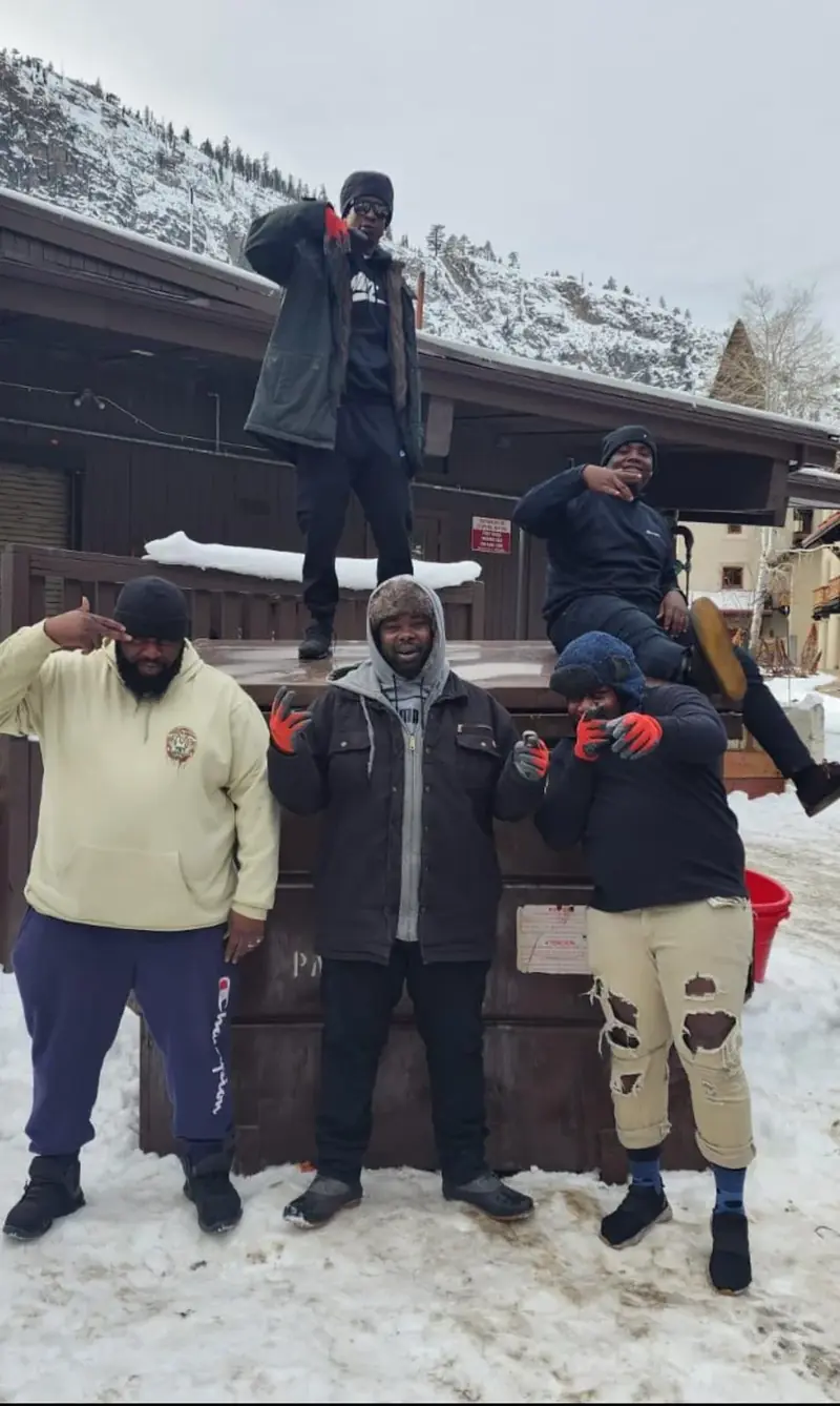 Five Yardie Cleaning team members in winter gear pose outdoors in snowy mountain town after a job